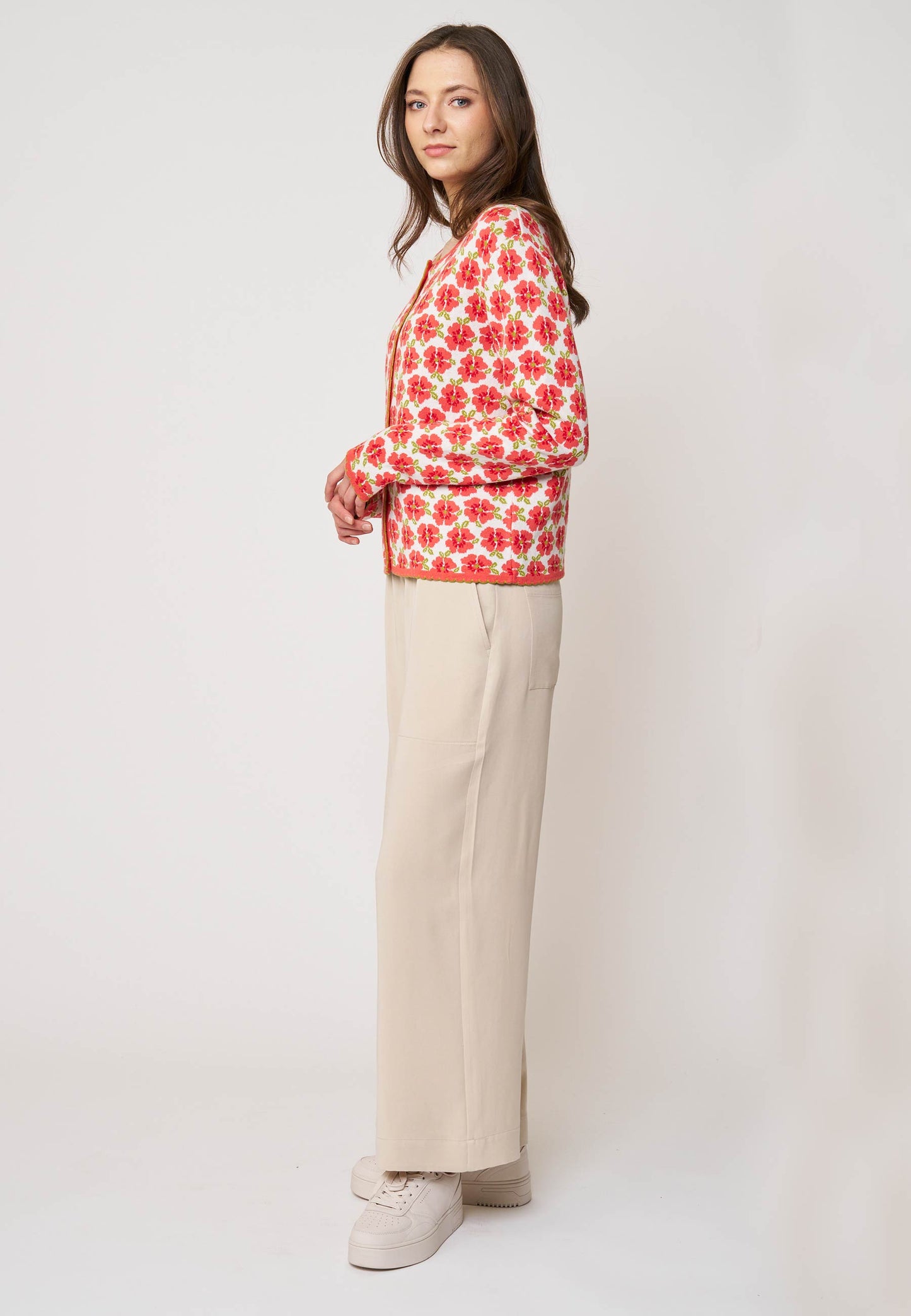 Frau trägt Strickjacke, Modell Juliana, mit korallrotem Blumenmuster auf beige Grund in Seitenansicht vor hellem Hintergrund
