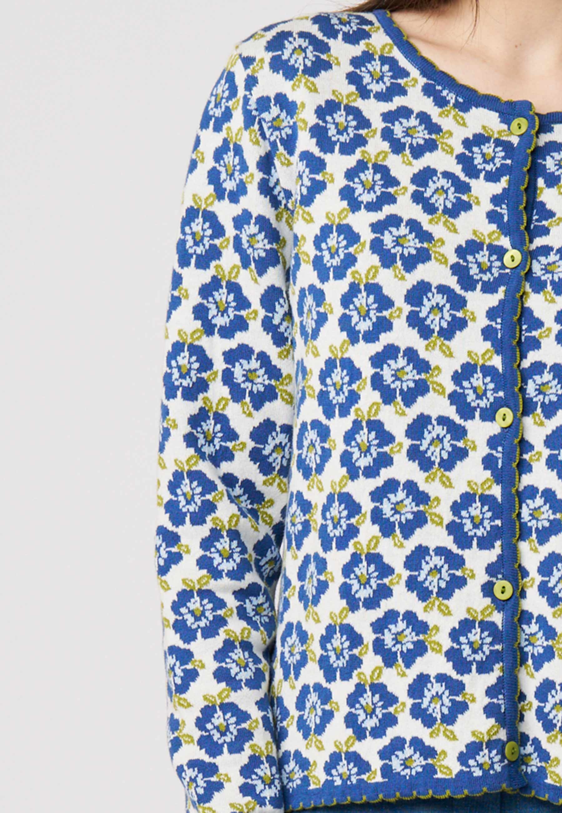 Frau trägt Strickjacke, Modell Juliana, mit blauem Blumenmuster und grünen Akzenten auf hellem Grund.