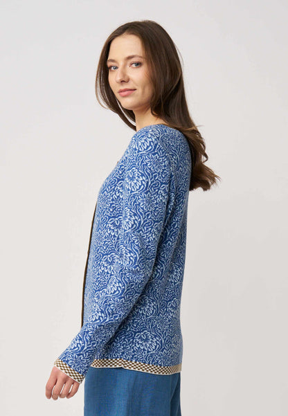 Frau im Profil trägt Strickjacke, Modell Lena, in Blau mit floralem Muster und kontrastierendem Saum vor hellem Hintergrund
