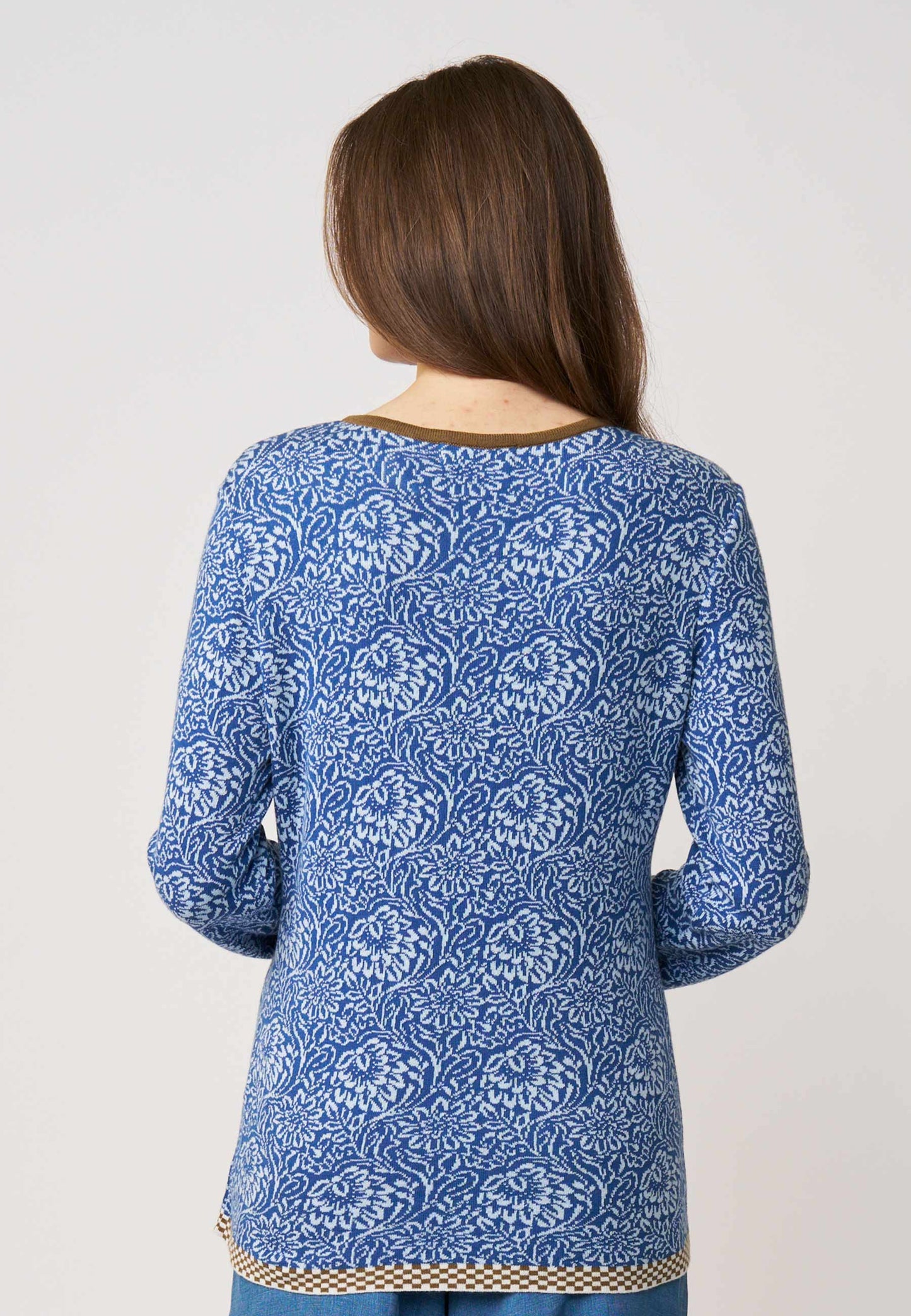 Frau trägt Strickjacke, Modell Lena, in Blau mit weißem floralen Muster und kontrastierendem Saum vor hellem Hintergrund