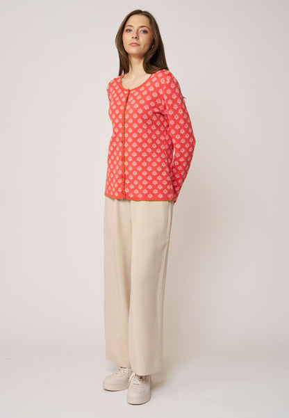 Frau trägt Strickjacke, Modell Lena, in Korallrot mit kleinem floralen Muster und rundem Ausschnitt vor hellem Hintergrund