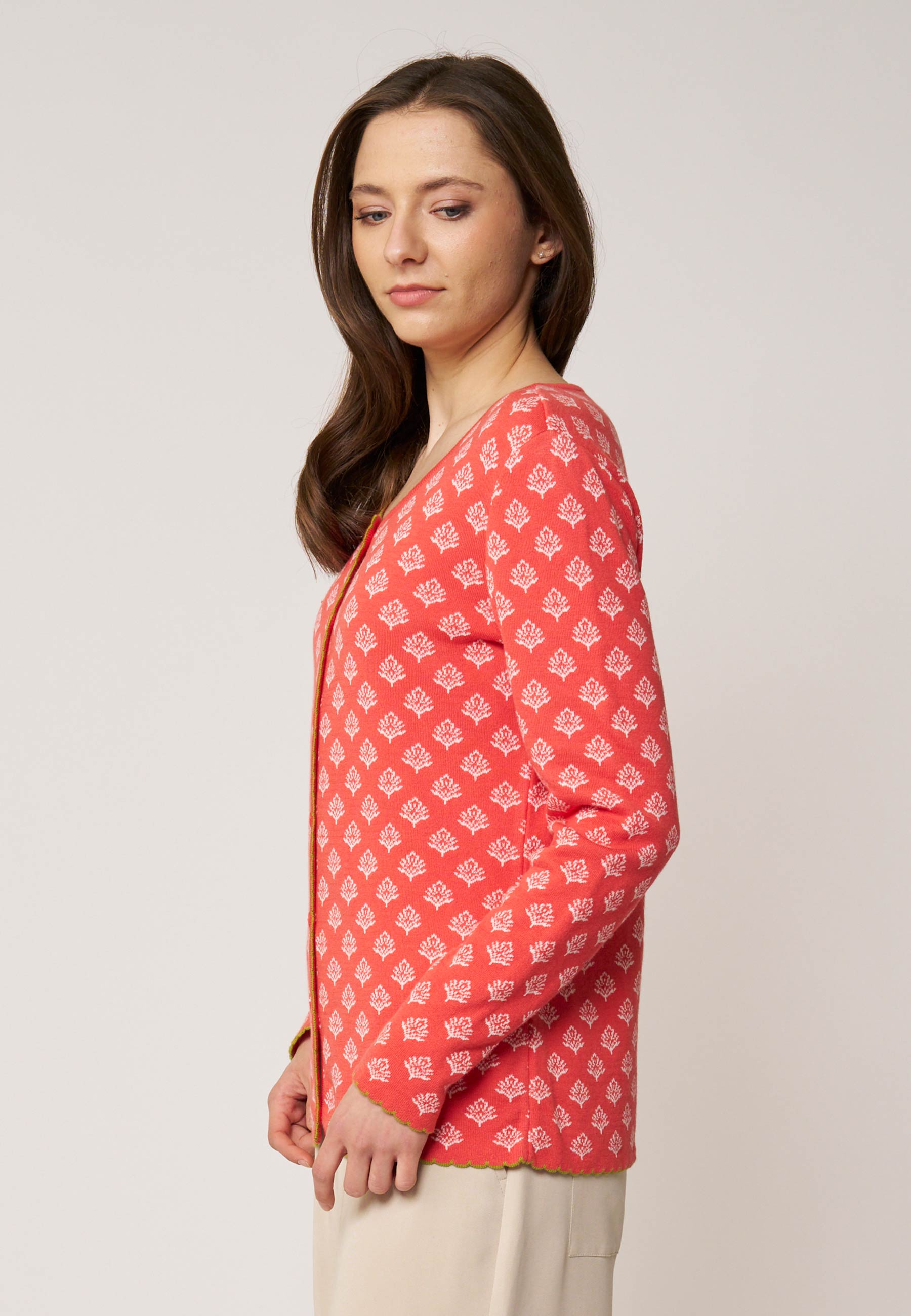 Frau trägt Strickjacke, Modell Lena, in Koralle mit weißem Muster und langem Arm vor hellem Hintergrund