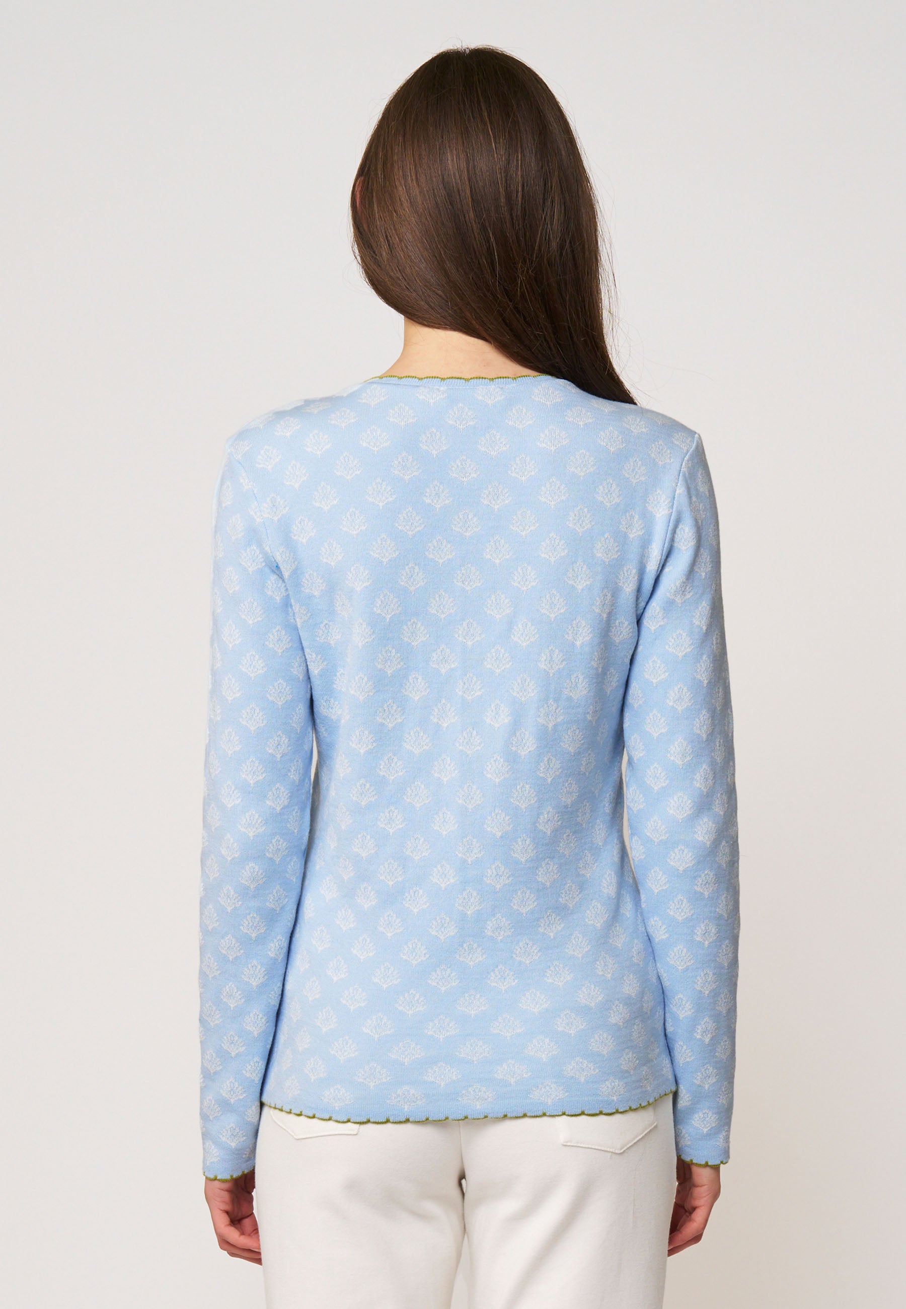 Frau trägt Strickjacke, Modell Lena, in Hellblau mit zartem Muster und grünem Zierband am Saum, Rückansicht