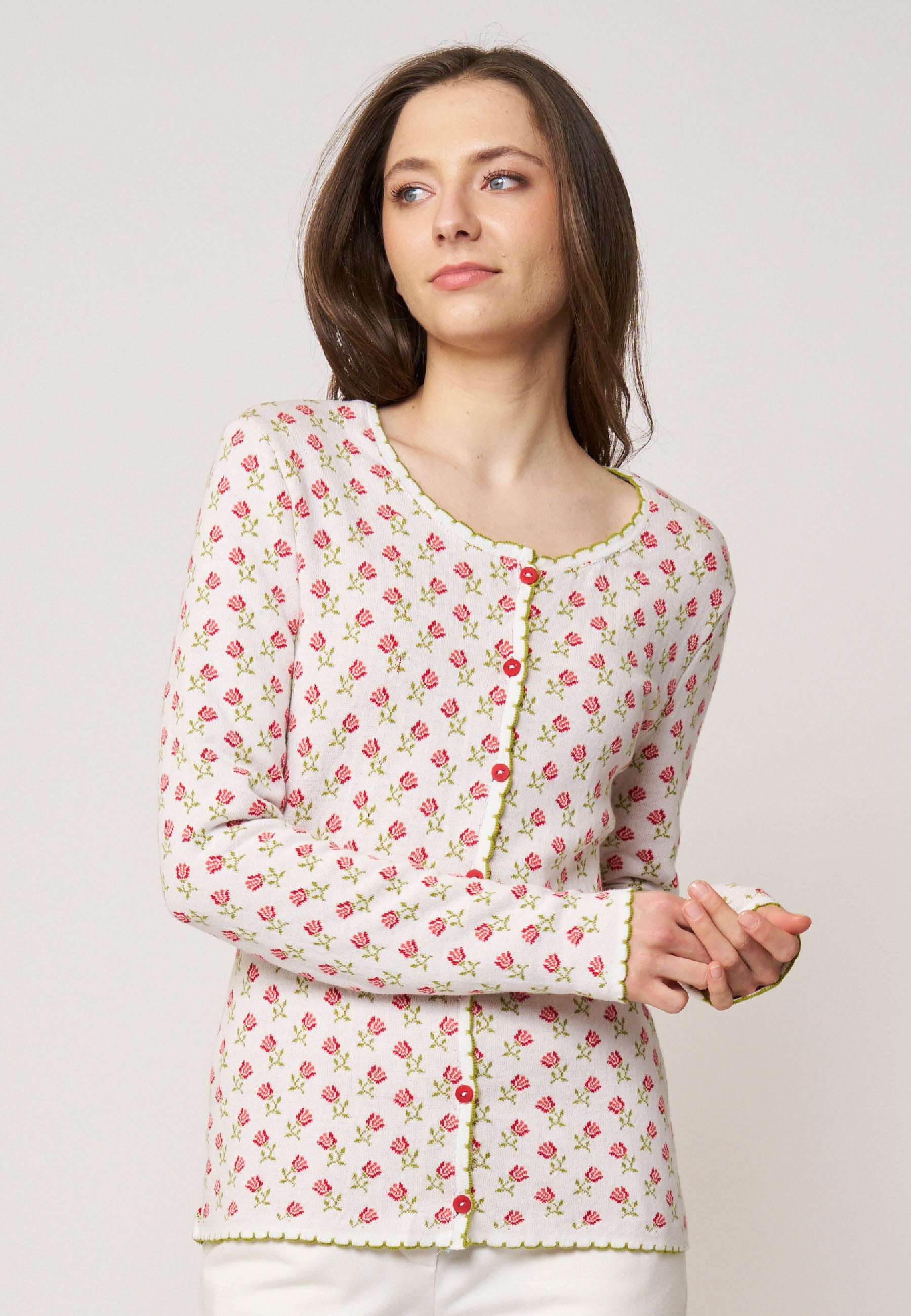 Frau trägt Strickjacke, Modell Lena, in hellem Ecru mit kleinem rosa Blumenmuster und grünem Zierstreifen frontal