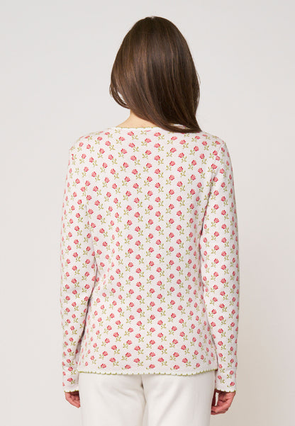 Frau trägt Strickjacke, Modell Lena, in Cremeweiß mit dezentem rosa Blumenmuster, Rückansicht vor hellem Hintergrund