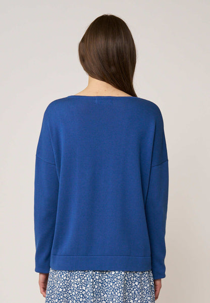 Frau mit braunem langen Haar trägt locker sitzenden, unifarbenen blaugrünen Pullover mit geradem Schnitt von hinten betrachtet