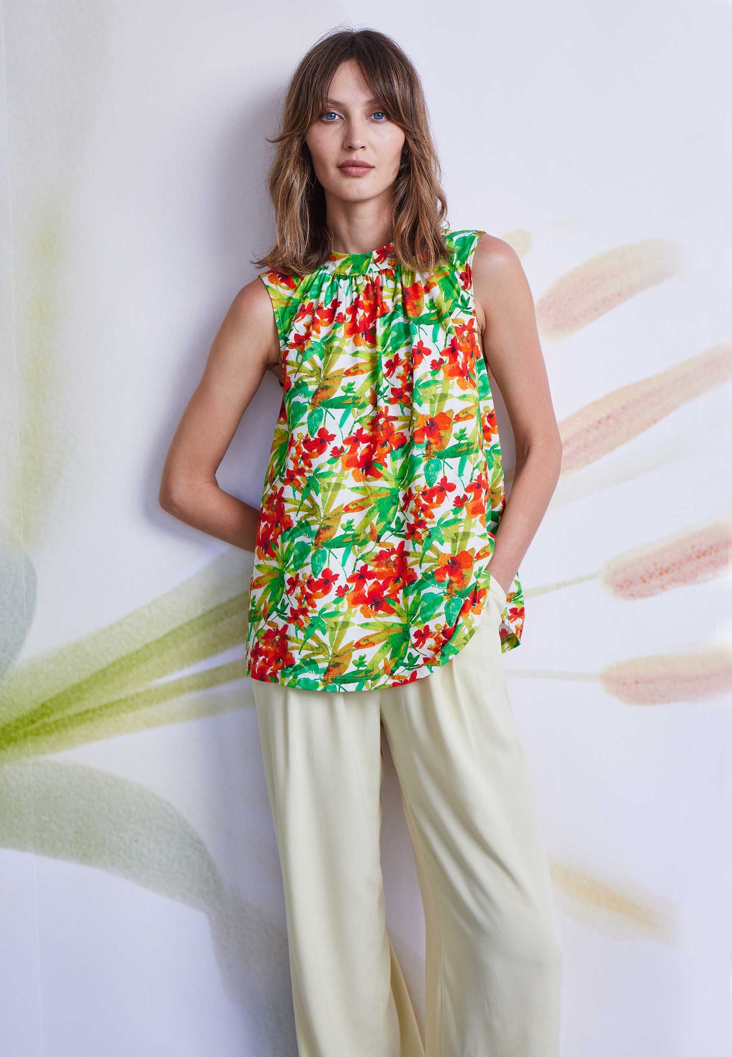 Frau trägt Top, Modell Ferra, mit floralem Muster in Rot- und Grüntönen und lockerem Schnitt vor Wand mit Musterung
