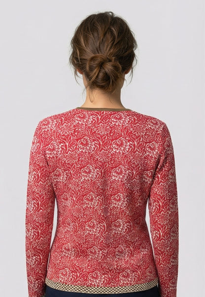 Frau trägt Strickjacke, Modell Lena, in Rot mit weißem floralen Muster und kontrastierendem Saum, Rückansicht.